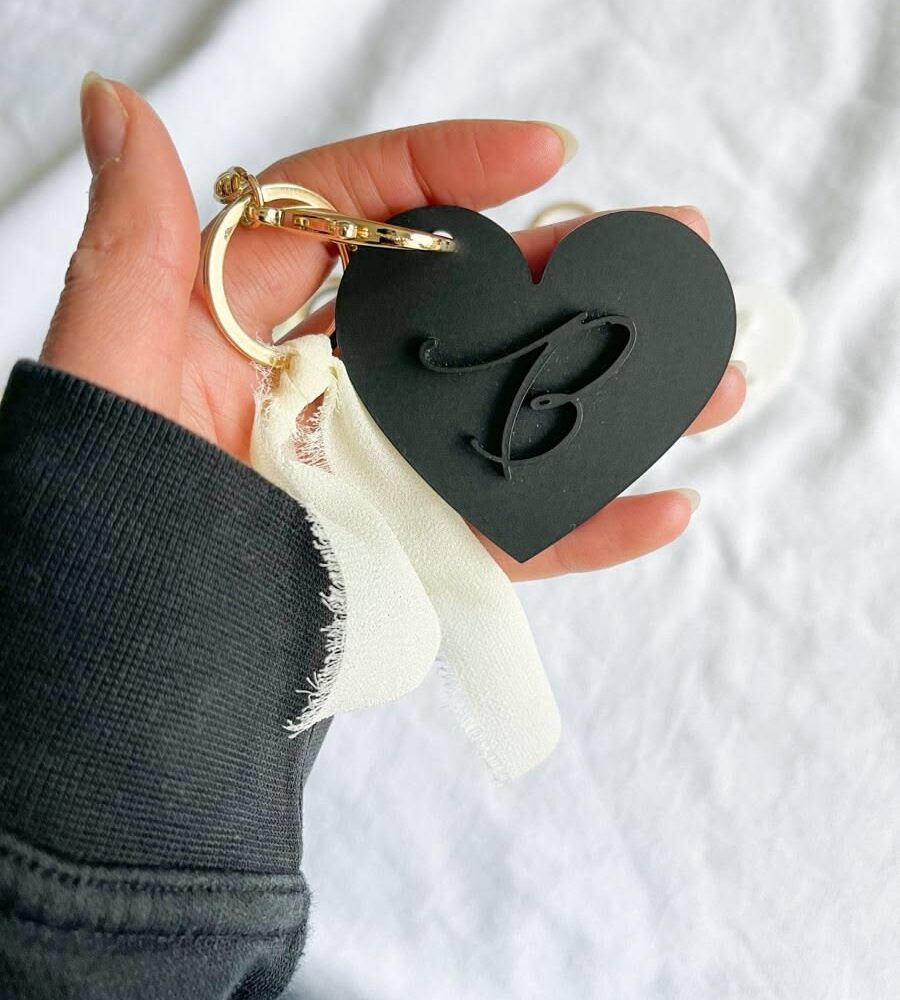 Black heart-shaped keychain with a raised initial and gold-coloured ring