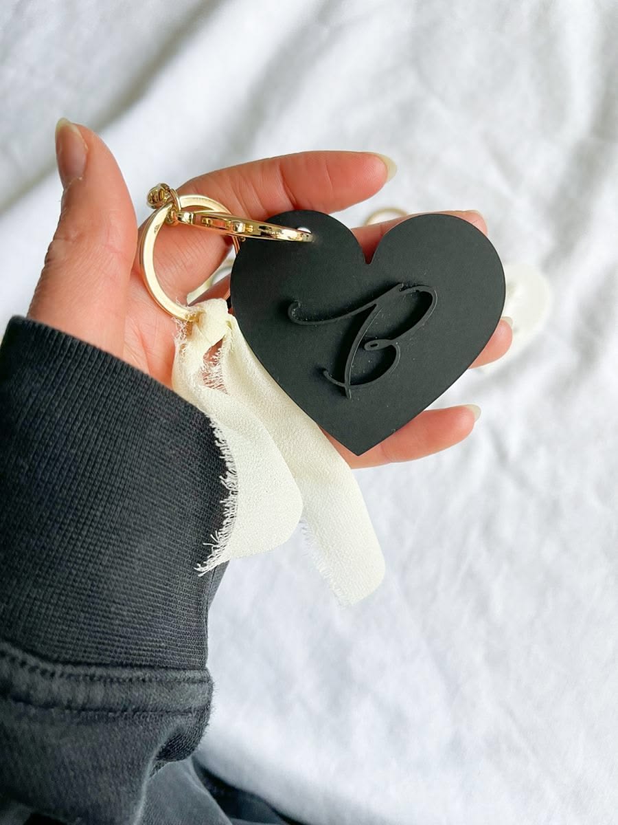 Black heart-shaped keychain with a raised initial and gold-coloured ring
