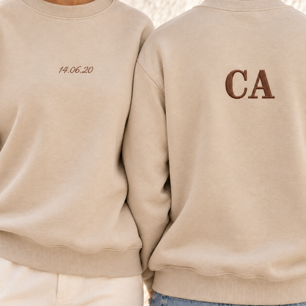 Close-up of matching beige sweatshirts with a small brown embroidered date on the front and larger CA initials on the back